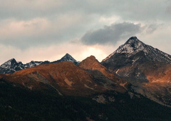 Breathtaking view of mountain peaks adorned with snow under a cloudy sky at dusk.